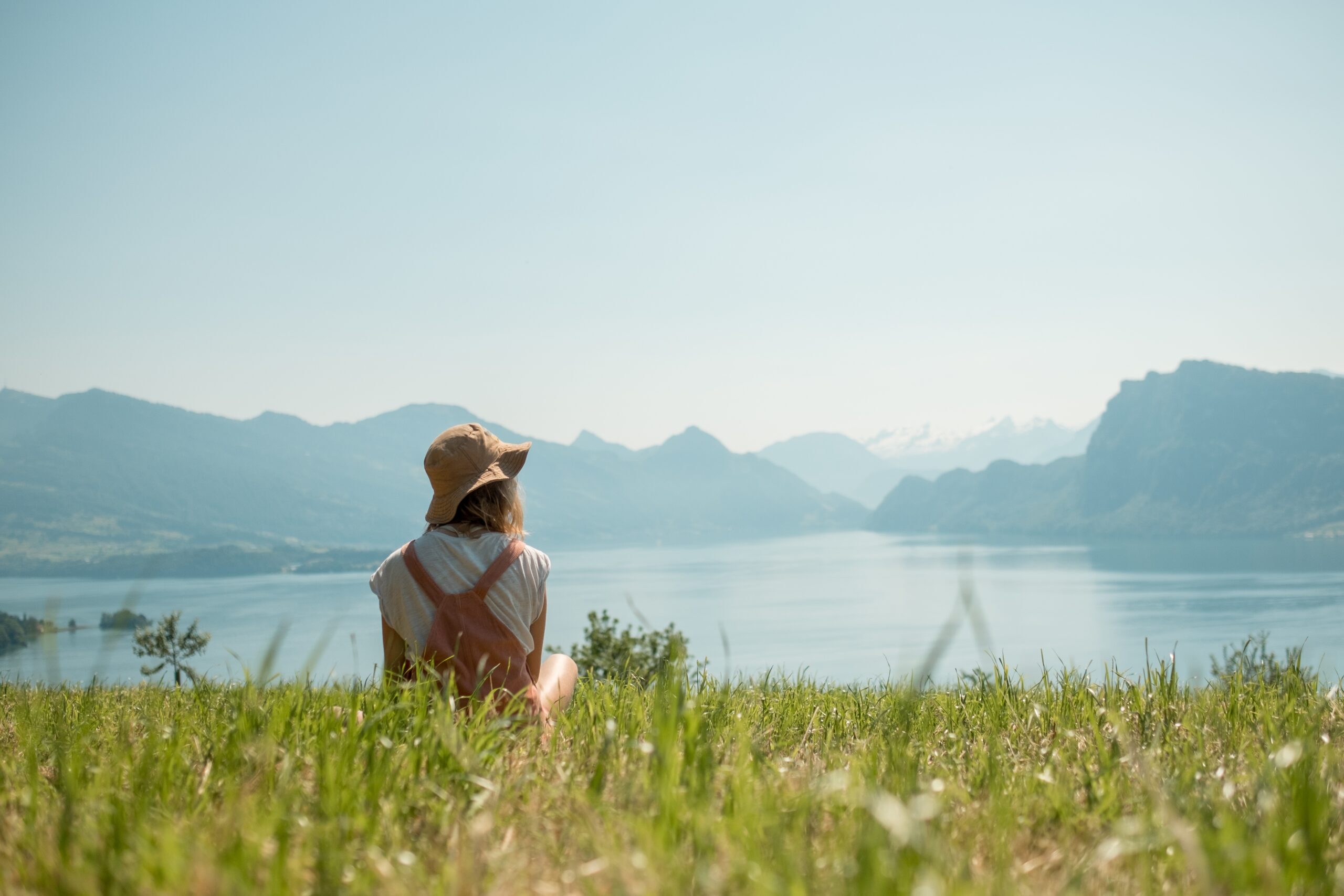 A girl with had sitting on the green lawn near the lake